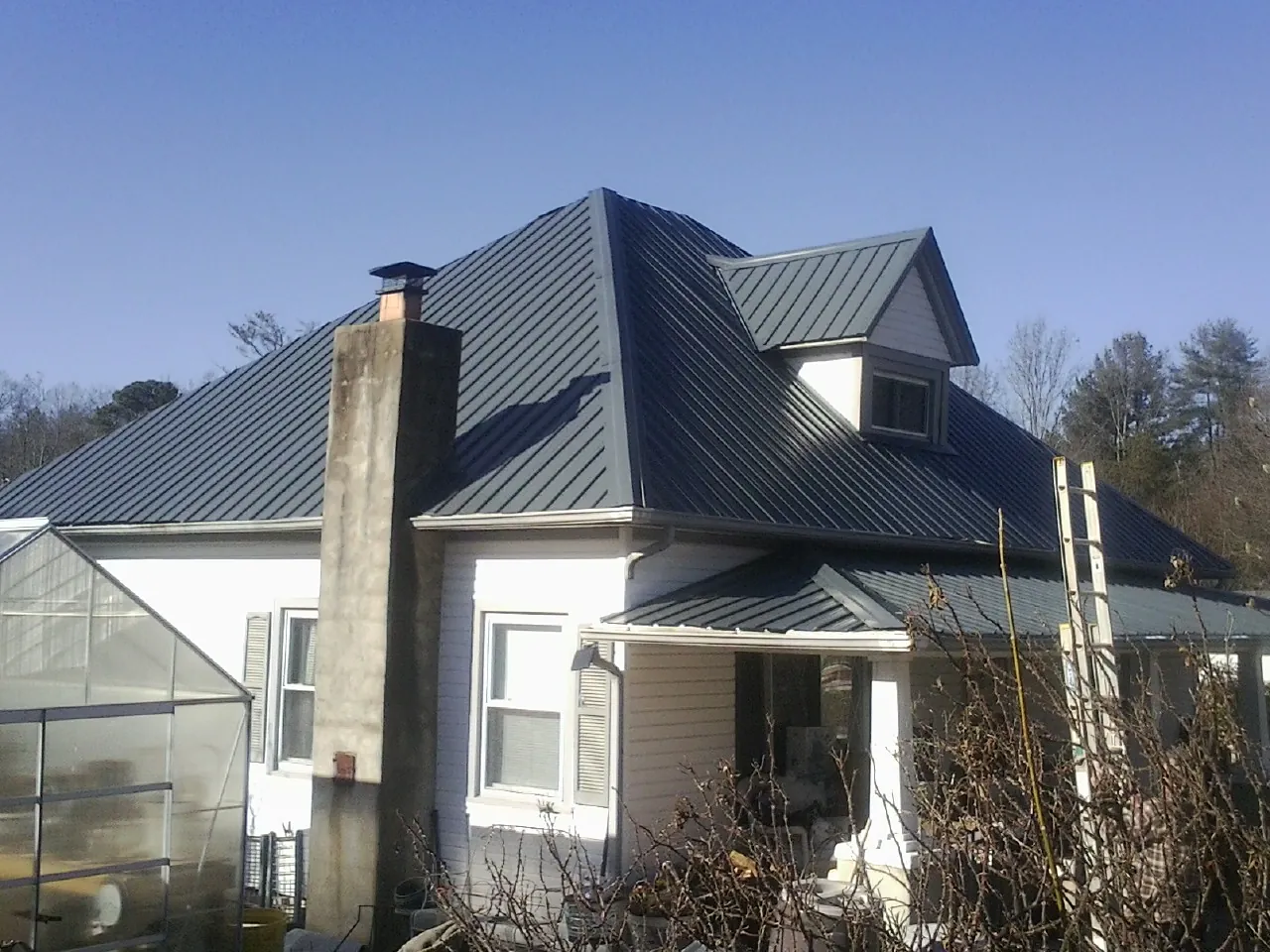 Dark blue standing seam metal roof on a white farmhouse with dormer — Slate & Tile Roof Repair by Roofing Brothers in Rosman
