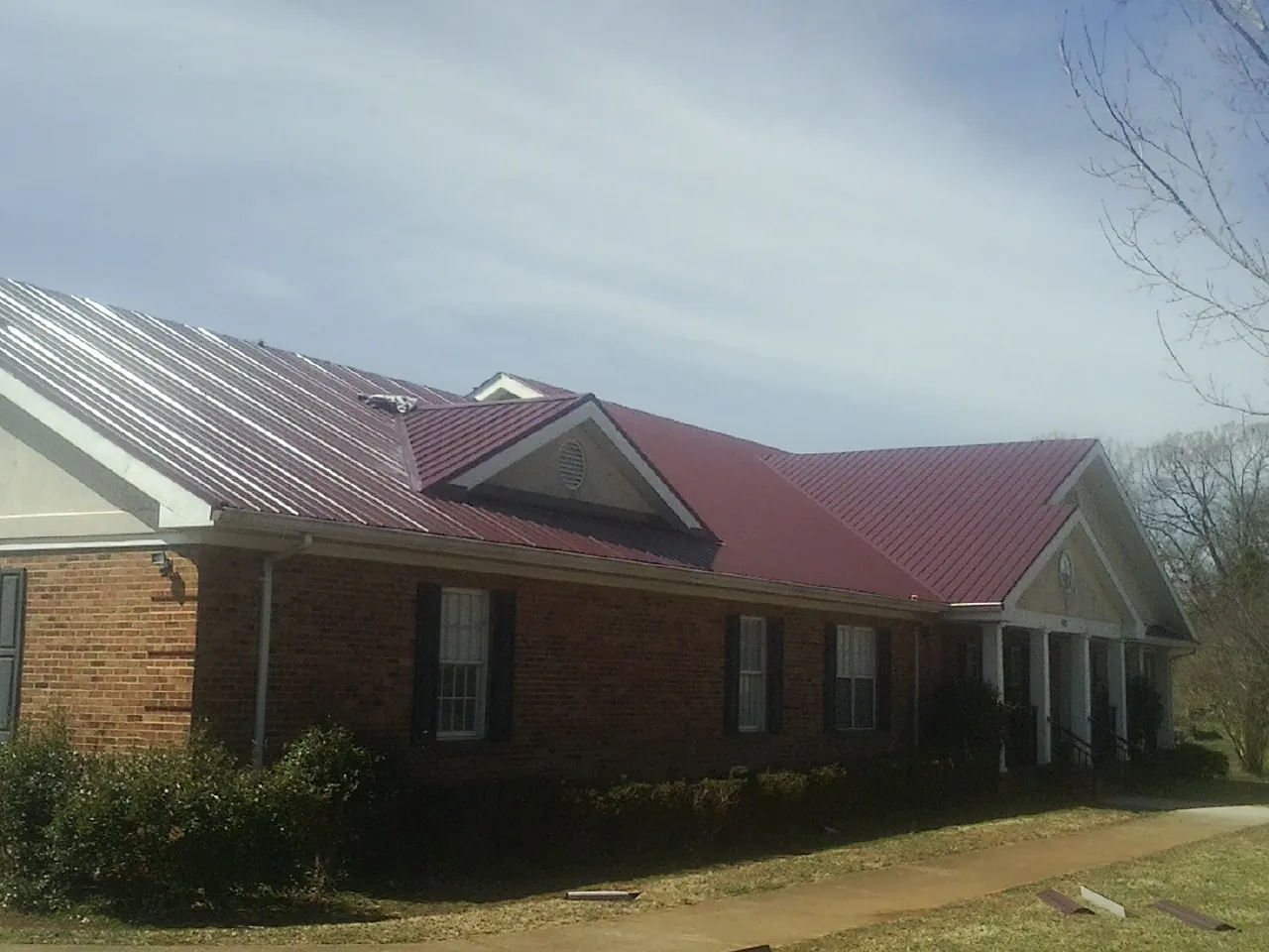Red metal roof with gabled entries on a long brick building, from a Hail Damage Roof Repair job in Rosman