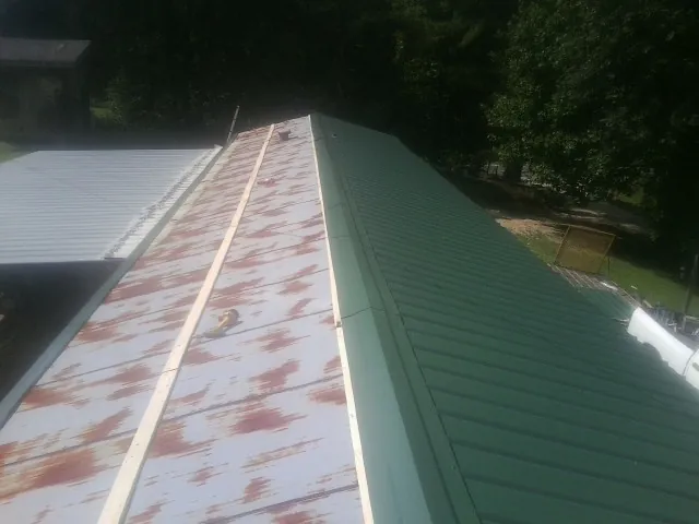 Old rusted panels beside newly installed green metal roofing — Wind Damage Roof Repair by Roofing Brothers in Rosman