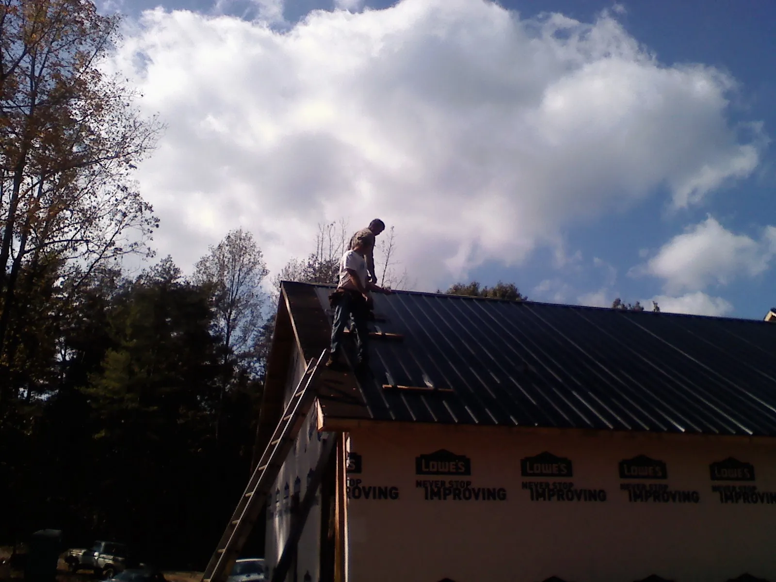 Roofer fastening dark metal panels high against a cloudy sky in Rosman