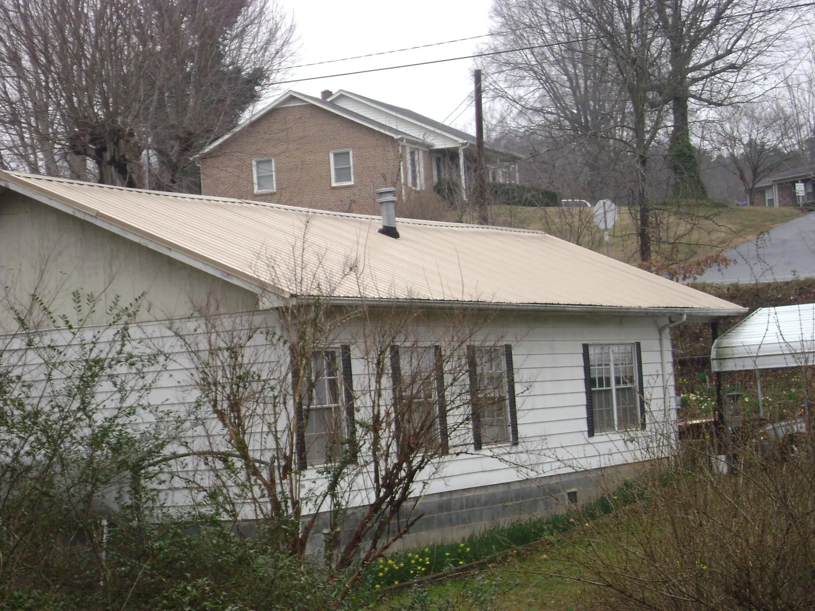 Tan metal roof on a white sided house set into a hillside — Commercial Roofing by Roofing Brothers in Rosman