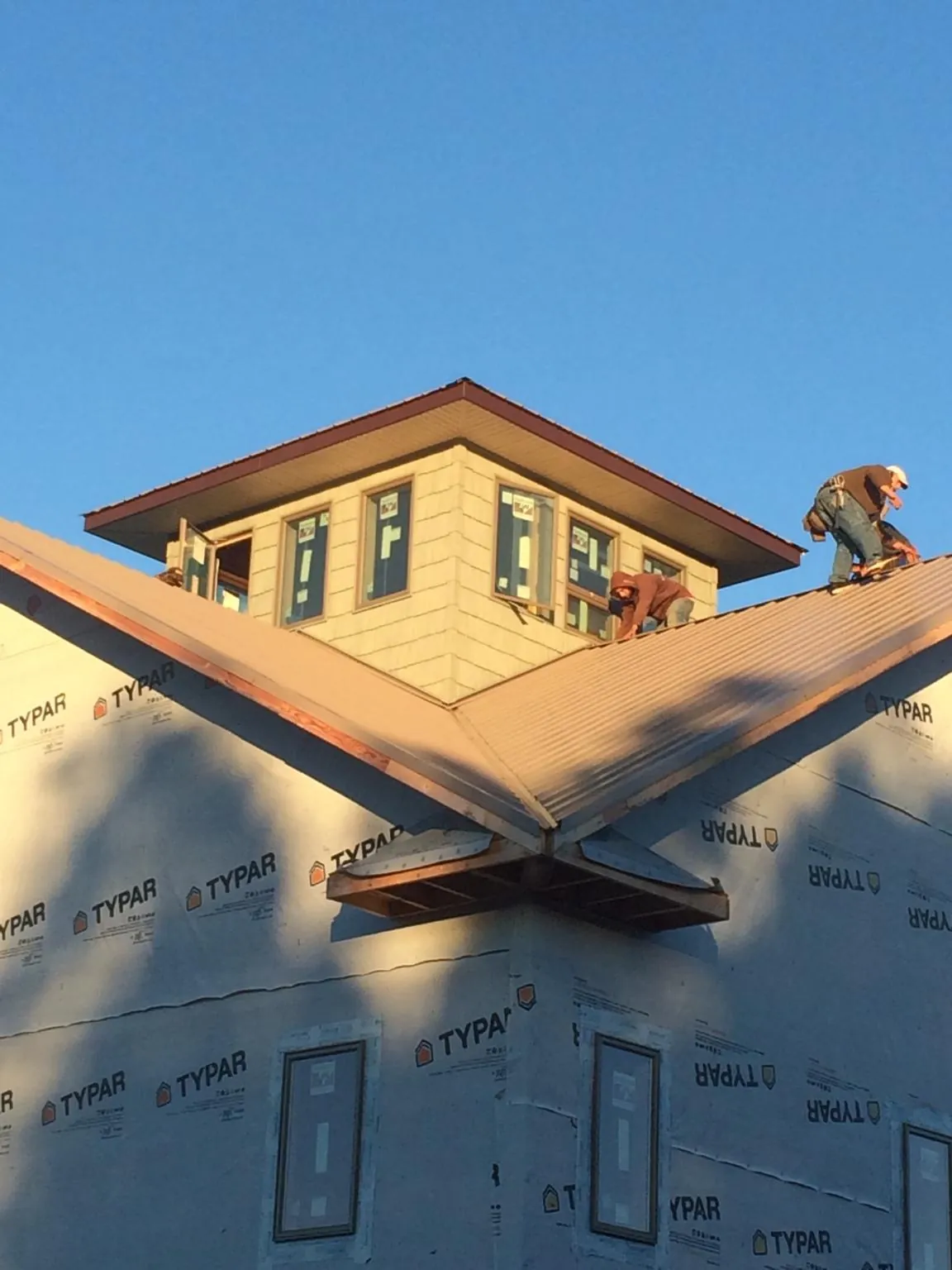 Roofers working around a rooftop cupola on a new metal roof at sunset — Roof Waterproofing in Rosman by Roofing Brothers